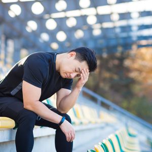 Frustrated Asian male athlete depressed, dissatisfied with the result of his training, in despair after running, resting sitting