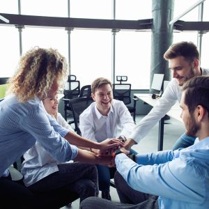 Businesspeople putting their hands on top of each other in nice light workstation, wearing casual clothes. Conception of successful teambuilding.